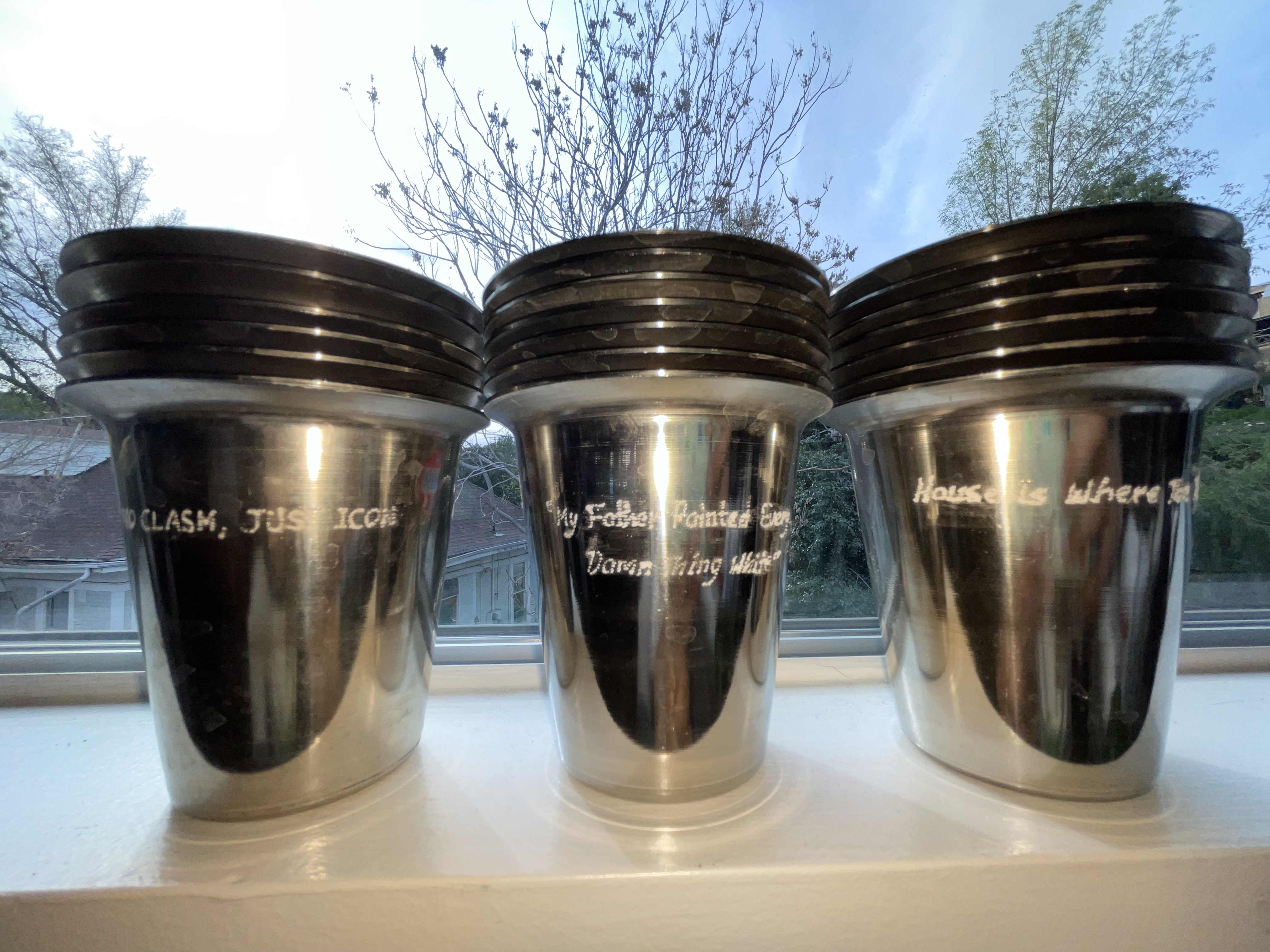 many silver tumblers are in three stacks. the tumblers have different phrases engraved on them